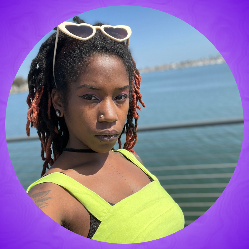 A Black woman with black and red dreadlocks in a neon green shirt.