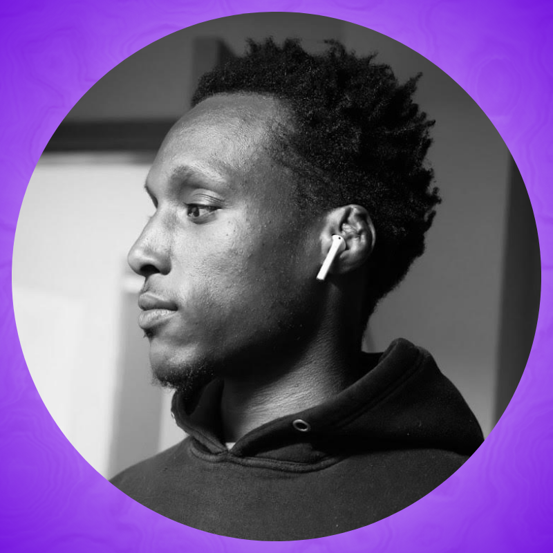 Black and white portrait of Brooks standing to the side, looking away from the camera, unsmiling. He’s wearing a dark hoodie and a wireless earbud is visible in his ear.