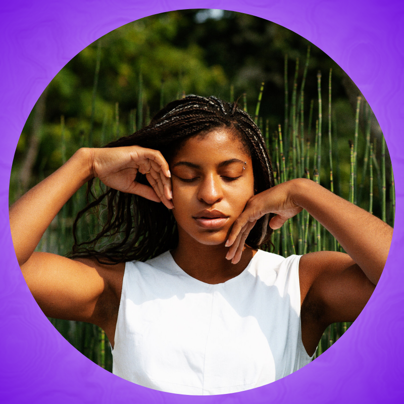 Portrait of Jhia outside with her eyes closed and hands caressing her face.