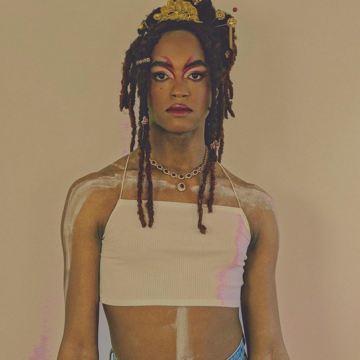 Painterly portrait of the artist Diovanna LáBeija. She is an afrolatina transfemme, and she is shown here in a gold crown, facing the camera directly, with pink and red dramatically lined eyebrows, red lipstick, unsmiling and regal.