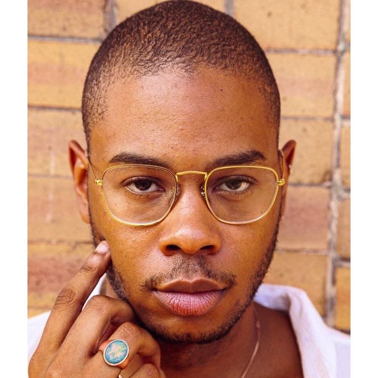 Headshot of the artist Carlton V. Bell, a Black queer person facing the camera. they wear thin-framed gold glasses and a white shirt.